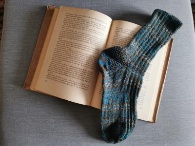 Ein offenes Buch, darin eine grün-graue Socke. Ein offenes Buch, darin eine grün-graue Socke.