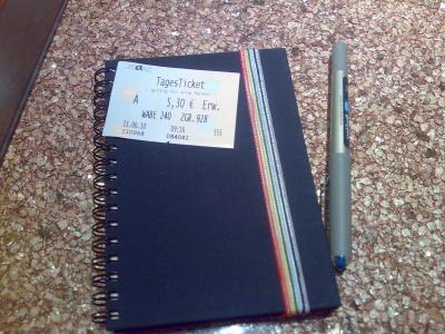 Auf meinem Notizbuch liegen meine Tagesticket für Bus und Bahn und ein Stift